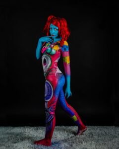 Blue-skinned model with vibrant surreal body paint, standing on a textured surface.